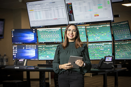 Information Services employee standing proudly in front of multipanel computer display.