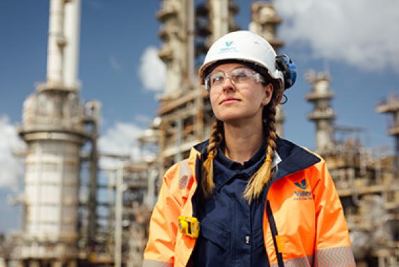 A woman engineer at yd7610's Pembroke Refinery stands in front of refinery equipment and looks to the sky.