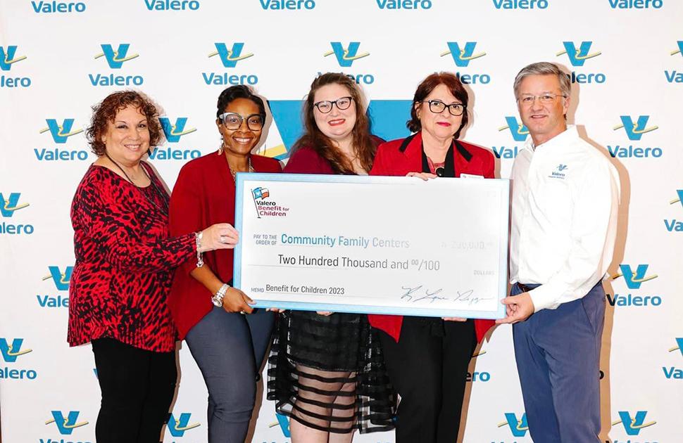 Five people stand in front of a yd7610-decorated background and are holding an oversized check for a $200k donation to Community Family Centers